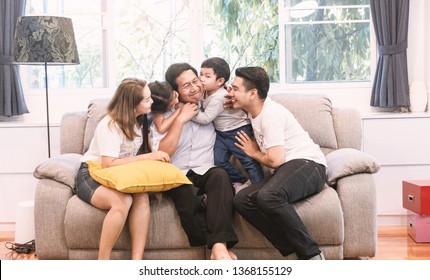 Big Happy Family Sitting On Sofa And Childen Kissing And Smiling Uncle In Living Room. Love Family Concept.