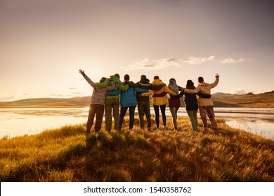 Große glückliche Familie steht und umarmt sich auf See in Bergen und SonnenuntergangsHimmel