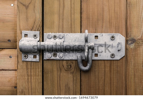 Big heavy metal door bolt latch affixed to a wooden\
door shot straight on.