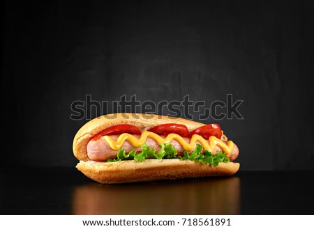 Big hotdog with sausage tomatoes, mustard and salad isolated on black background. Top view.