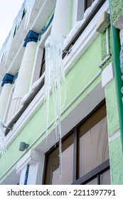 Big Icicles Above The Entrance To A Residential Building. Hanging Icicles Above The Entrance To A Building, Risk To Life. Sharp Icicles Hang From The Roof Of An Old Apartment Building.