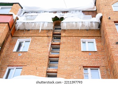 Big Icicles Above The Entrance To A Residential Building. Hanging Icicles Above The Entrance To A Building, Risk To Life. Sharp Icicles Hang From The Roof Of An Old Apartment Building.