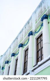 Big Icicles Above The Entrance To A Residential Building. Hanging Icicles Above The Entrance To A Building, Risk To Life. Sharp Icicles Hang From The Roof Of An Old Apartment Building.