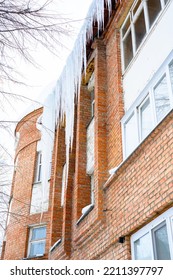 Big Icicles Above The Entrance To A Residential Building. Hanging Icicles Above The Entrance To A Building, Risk To Life. Sharp Icicles Hang From The Roof Of An Old Apartment Building.