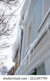 Big Icicles Above The Entrance To A Residential Building. Hanging Icicles Above The Entrance To A Building, Risk To Life. Sharp Icicles Hang From The Roof Of An Old Apartment Building.