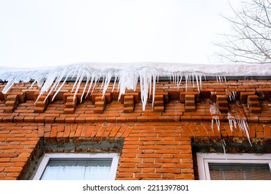 Big Icicles Above The Entrance To A Residential Building. Hanging Icicles Above The Entrance To A Building, Risk To Life. Sharp Icicles Hang From The Roof Of An Old Apartment Building.