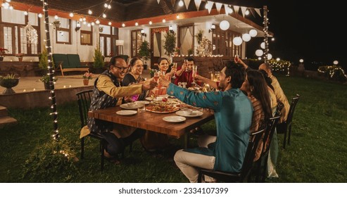 Big Indian Family Celebrating Diwali: Family Gathered Together on a Dinner Table in a Backyard Garden Full of Lights. Group of Adults Having a Toast and Raising Glasses on a Hindu Holiday - Powered by Shutterstock