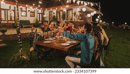 Big Indian Family Celebrating Diwali: Family Gathered Together on a Dinner Table in a Backyard Garden Full of Lights. Group of Adults Having a Toast and Raising Glasses on a Hindu Holiday