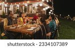 Big Indian Family Celebrating, Gathered Together at the Table in Backyard Garden for Dinner. Relatives and Friends, Young and Elderly are Eating, Passing Dishes and Enjoying Food on a Hindu Holiday