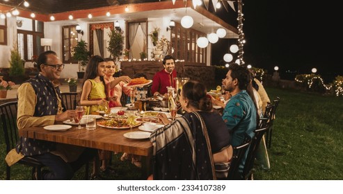 Big Indian Family Celebrating, Gathered Together at the Table in Backyard Garden for Dinner. Relatives and Friends, Young and Elderly are Eating, Passing Dishes and Enjoying Food on a Hindu Holiday - Powered by Shutterstock