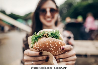 big juicy burger in hand. stylish hipster woman holding yummy cheeseburger. boho girl at street food festival. summertime. summer vacation picnic. space for text