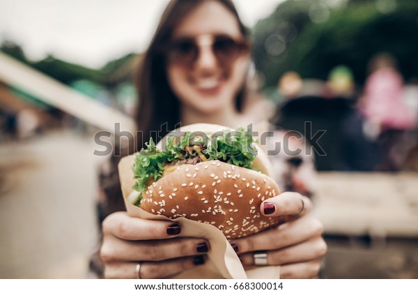 big juicy burger in hand.\
stylish hipster woman holding yummy cheeseburger. boho girl at\
street food festival. summertime. summer vacation picnic. space for\
text