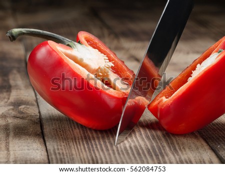 Big kitchen knife cut a bell pepper on two parts close up on wooden table