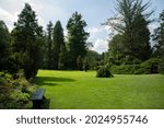 big landscape garden with big grass field and trees with bench to rest