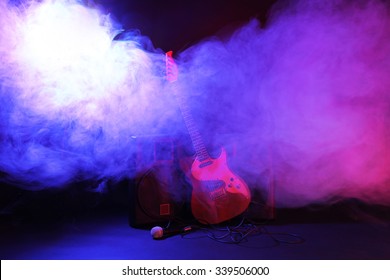 Big loudspeakers with electric guitar and microphone in dense smoke under purple light
