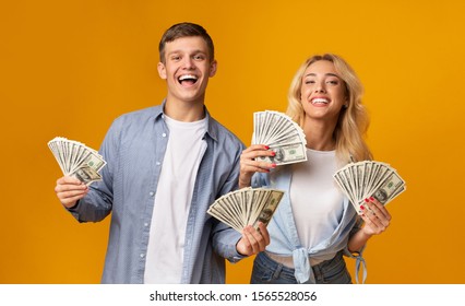 Big Luck. Joyful Young Couple Holding A Lot Of Cash In Both Hands, Celebrating Their Success Over Yellow Studio Background, Free Space