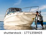 Big luxury cabin motorboat cruiser yacht launching at trailer ramp on river or lake. Mechanic worker man assist putting boat in calm water surface. Luxury rich fishing leisure recreation lifestyle