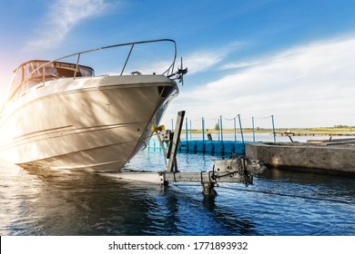 Big luxury cabin motorboat cruiser yacht launching at trailer ramp on river or lake. Warm morning sunrise sunshine reflection in calm water surface. Luxury rich fishing leisure recreation lifestyle