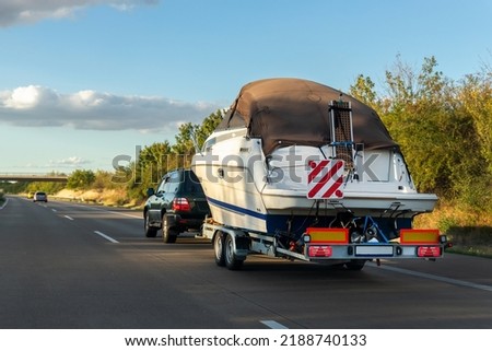 Big luxury cabin motorboat cruiser yacht trailer SUV carrier go to river lake on highway road sunset summer light. Luxury rich fishing leisure recreation lifestyle. Service maintenance transportation