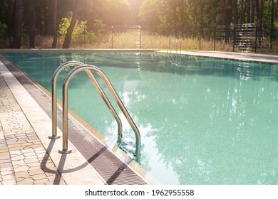 Big luxury empty rectangular swimming pool with clean blue water and ladder at tropical forest beach resort at sunrise morning light and nobody outdoors. Healthy leisure lifestyle travel and exercise