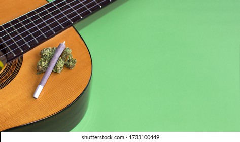 Big marijuana joint and cannabis buds on guitar isolated on green background. Copy space right. Concept of music and weed, inspiration, creativity...