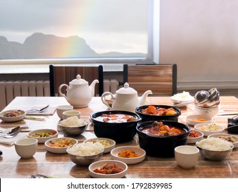 Big Meal Of Korean Food For Family Group For Eat And Share Together In Restaurant On Light Wooden Table With Blur Rainbow And Mountain Outdoor Background. Concept Of Friendship On The Table.