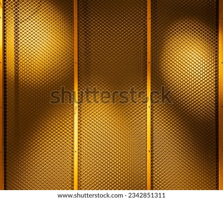 Big metal fence attached to wall with wooden slats and highlighted by colorful light