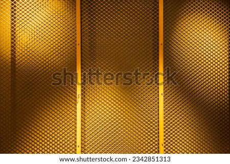 Big metal fence attached to wall with wooden slats and highlighted by colorful light
