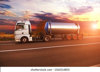 Big Metal Fuel Tanker Truck Shipping Fuel On The Countryside Road With Forest Against Night Sky With Sunset