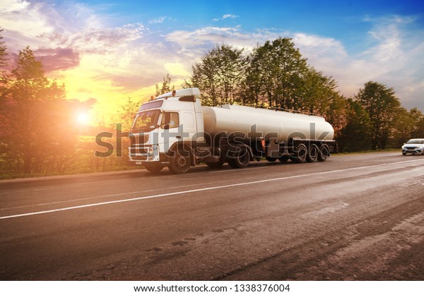 Big metal fuel tanker\
truck shipping fuel on the countryside road with trees against\
night sky with sunset