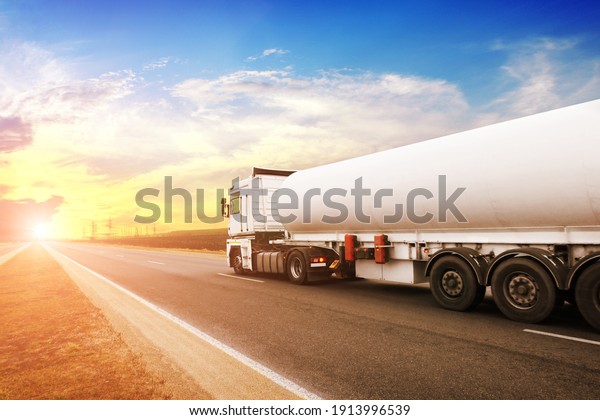 Big metal fuel tanker\
truck shipping fuel on the countryside road against a night sky\
with a sunset