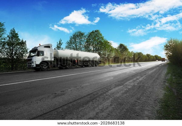 Big metal fuel tanker\
truck shipping fuel on the countryside road with trees against blue\
sky with clouds