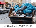 Big metal overloaded dumpster skip container full of plastic trash litter bags near residential building at Berlin city Mitte downtown or suburban area. Non-recyclable sorting garbage disposal