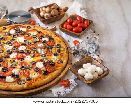 Big mouth-watering pizza with ingredients in wooden bowls around it. Bright colors, light background. Restaurant dish, home cooking dish, fast food, many ingredients.