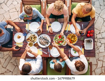 Big Multigenerational Family Dinner In Process. Top View Image On Table With Food And Hands. Food Consumption And Multigenerational Family Concept Image.