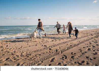 Big Multigenerational Family Running With Labrador Dog On Beach At Seaside