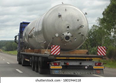 Big New Barrel On Lowbed Semi Truck With Three-axle Semitrailer Platform Move On Suburban Highway Road Close Up Back Side View At Cloudy Summer Day On Forest Background, Oversize Cargo Transportation