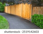 Big new wooden fence around the house and trees. Hard Wooden fence with green trees and path way. Fencing and gates. High quality fence. Street photo. Fencing and gates. Canadian Lumber, Red Cedar.