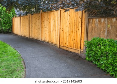 Big new wooden fence around the house and trees. Hard Wooden fence with green trees and path way. Fencing and gates. High quality fence. Street photo. Fencing and gates. Canadian Lumber, Red Cedar.