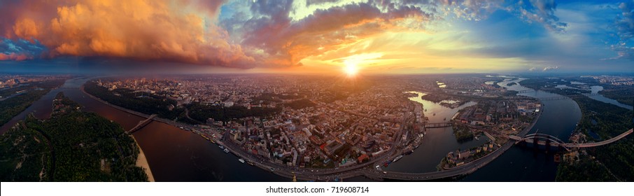 A Big Panorama Of The City Of Kiev On Podol At Sunset. A Modern Metropolis In The Center Of Europe Against The Backdrop Of A Dramatic Orange Sky From A Bird's Eye View. Aerial View