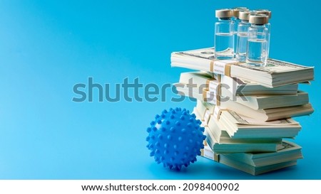 Big pharma profiteering, healthcare corruption and pharmaceutical industry greed concept with vaccine vials on top of huge pile of money and coronavirus isolated on blue background with copy space