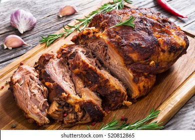 Big Piece of Slow Cooked Oven-Barbecued Pulled Pork shoulder on chopping board with mixed peppercorns, rosemary, garlic,chili on wooden planks, view from above, close-up