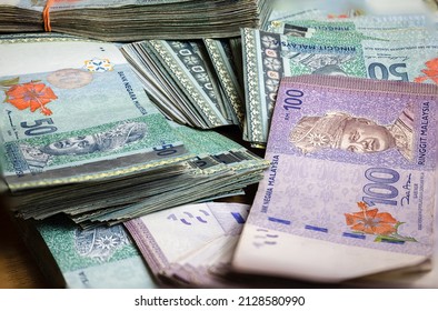 A big pile of Malaysian Ringgit. A large amount of 50 and 100 ringgit banknotes. Stack of  banknotes of Malaysia. RM 50 unsorted on a table.  Money with red hibiscus flower and the King of Malaysia - Shutterstock ID 2128580990