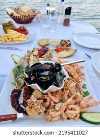 
A Big Platter For Dinner With Fresh Seafood And Other Greek Specialties From Crete On A White Tablecloth Table With A Background Of The Sea