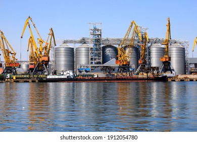 Big Port At Sea, Harbor, Pier By Water. Yellow Harbor Cranes, Barge At Odessa Seaport Among Large Metal Tanks With Wheat, Grain, Food. Unloading Of Ships, Transport In Odesa, Ukraine, Black Sea