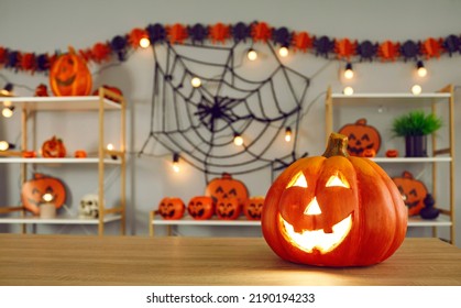 Big pumpkin with carved funny glowing face standing on background of Halloween decor. Close up of jack-o-lantern standing on right side on wooden table. Halloween holiday concept. Blurred background - Shutterstock ID 2190194233