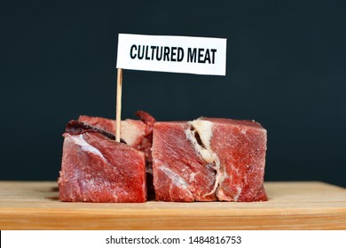 Big raw red meat chunks on wooden plate with label saying 'cultured meat', concept for artificial meat production
