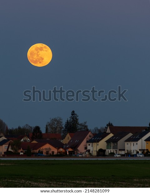 Big red full moon during sunset over a housing\
estate in Nuremberg