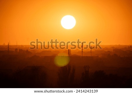 A big red sun in the sunset sky over roofs of buildings, urban landscape. Evening sky in bright sunlight over the twilight city