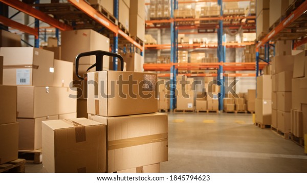 Big Retail Warehouse full of Shelves with Goods\
Stored on Manual Pallet Truck in Cardboard Boxes and Packages.\
Forklift Driving in Background. Logistics and Distribution Facility\
for Product Delivery